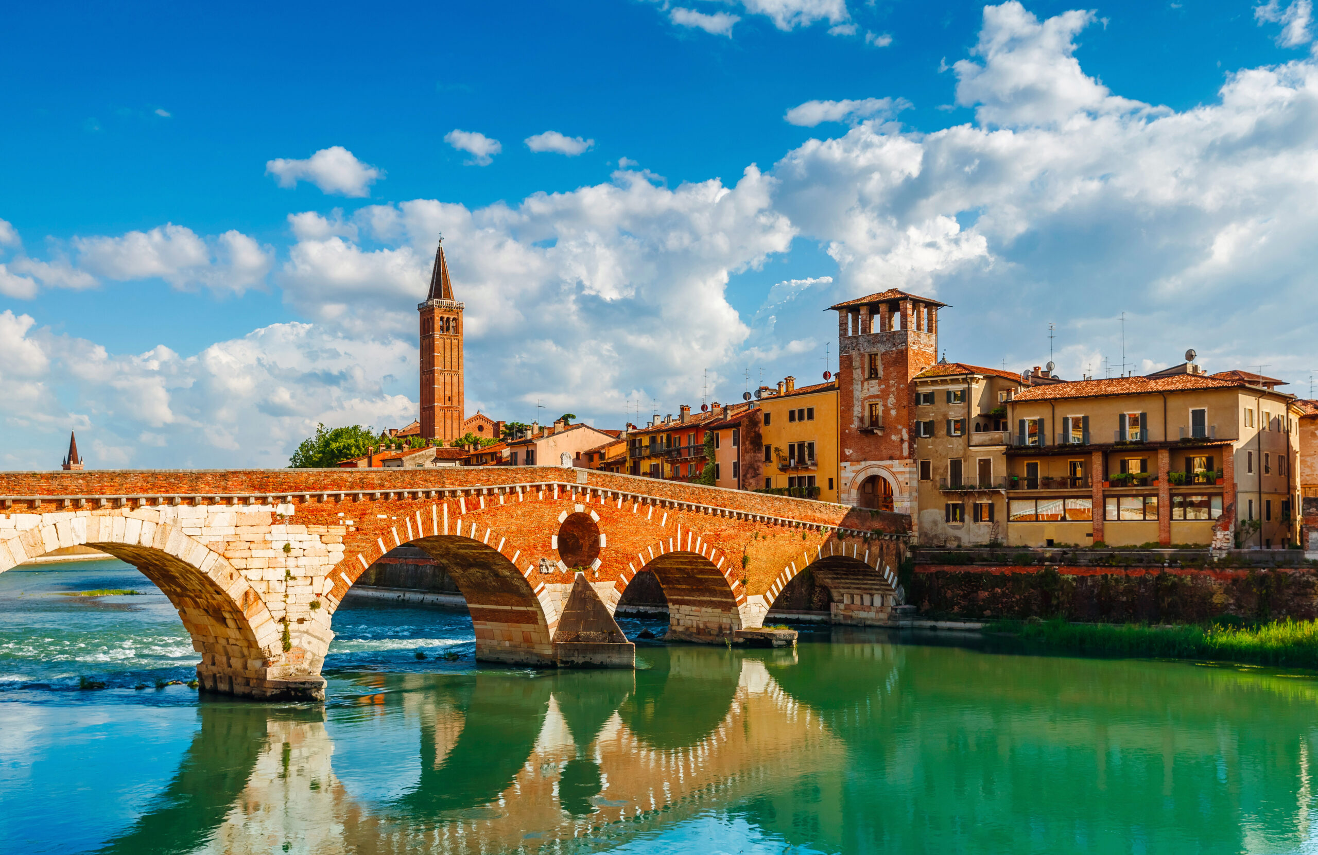 Bridge Ponte Pietra in Verona on Adige river. Veneto region. Italy. Sunny summer day panorama and blue sky with clouds. Ancient european terracotta color houses