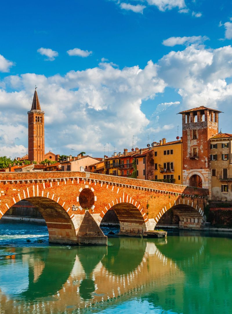 Bridge Ponte Pietra in Verona on Adige river. Veneto region. Italy. Sunny summer day panorama and blue sky with clouds. Ancient european terracotta color houses